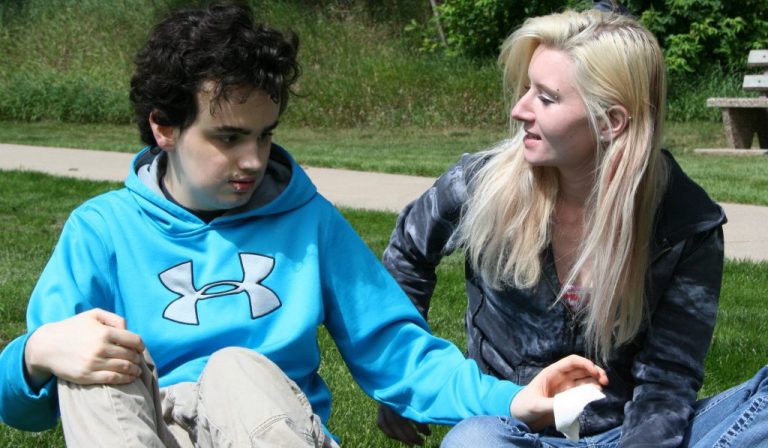 A woman who works as a Direct Support Professional sits next to an adolescent boy who has disabilities.