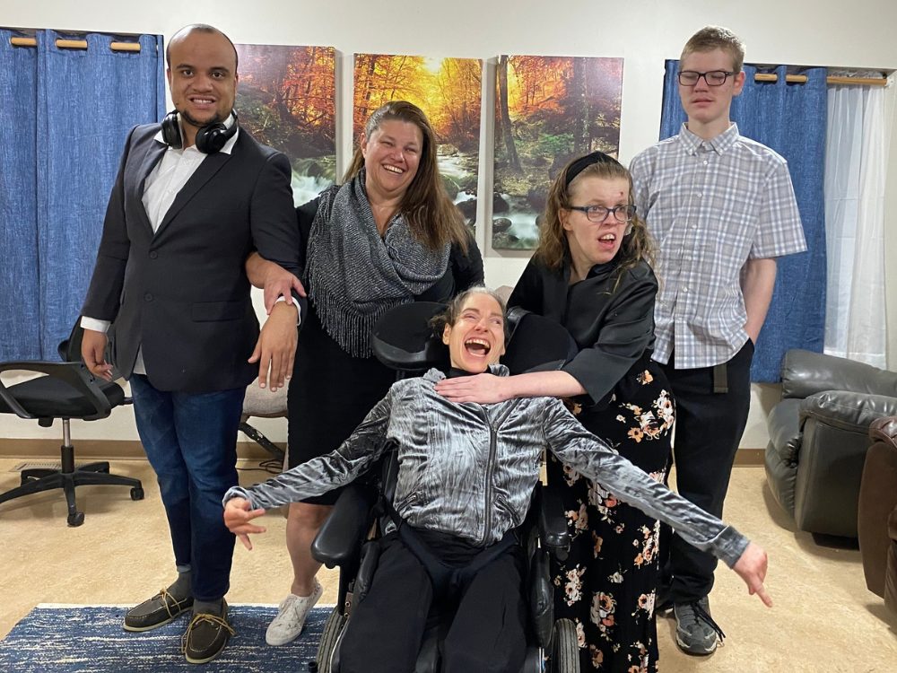 Two men and two women stand behind a woman in a wheelchair. All are smiling.