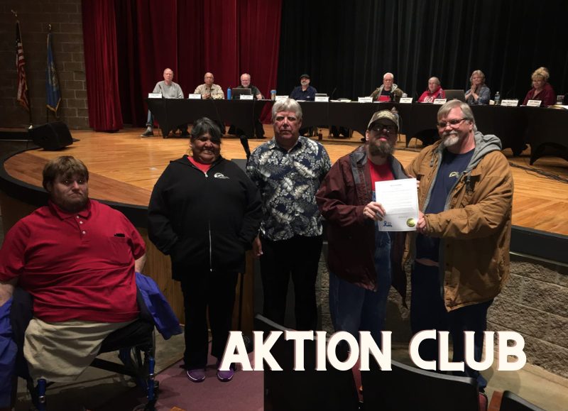 Three men, one woman, and a man in a wheelchair stand together in front of a stage at a community meeting in Hot Springs, South Dakota.